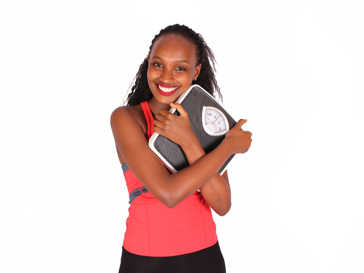 person standing on a scale with a measuring tape and fruits around, symbolizing weight loss and health